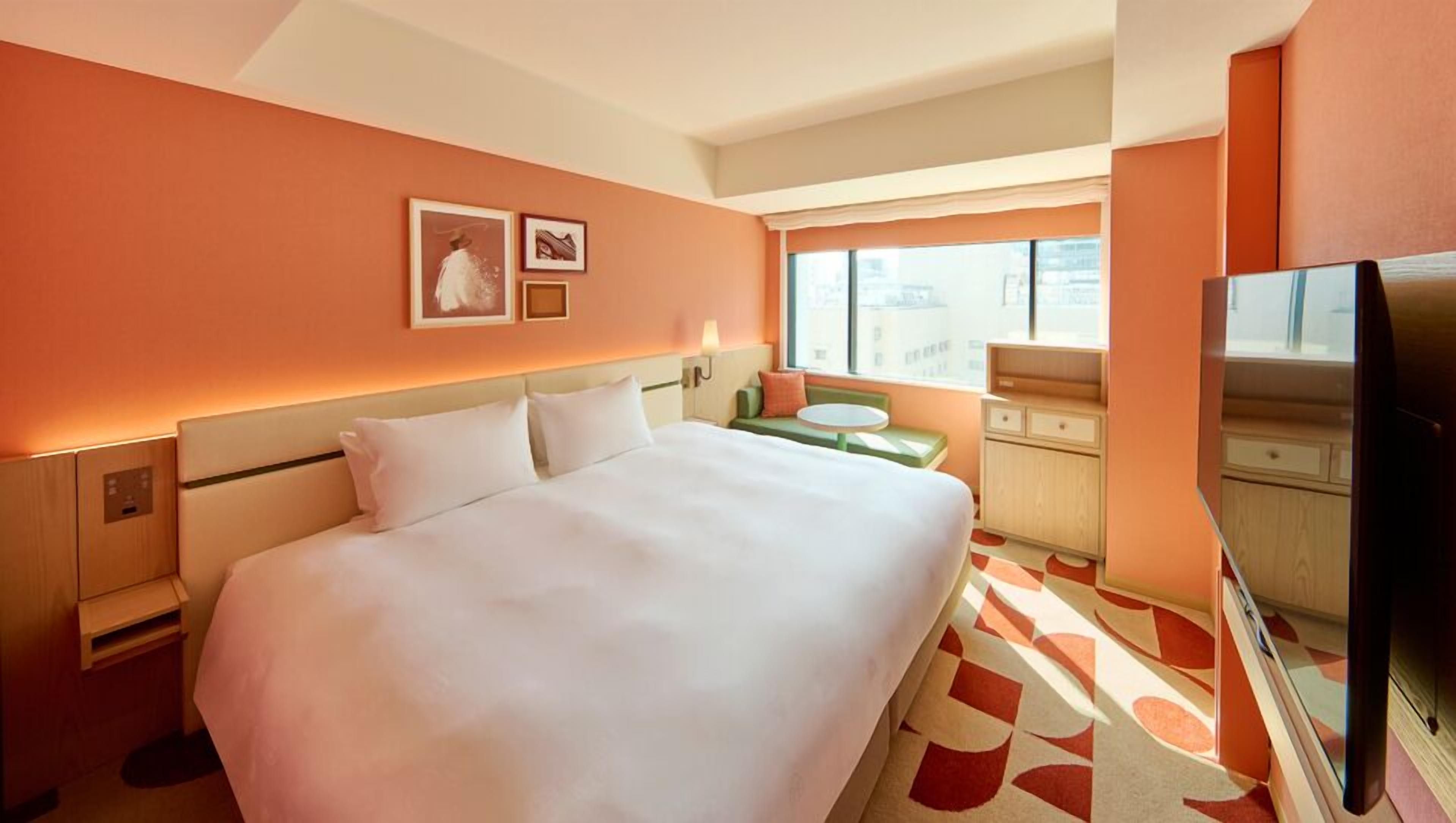 A hotel room with a large bed, a television, a small table, and a window with a city view.