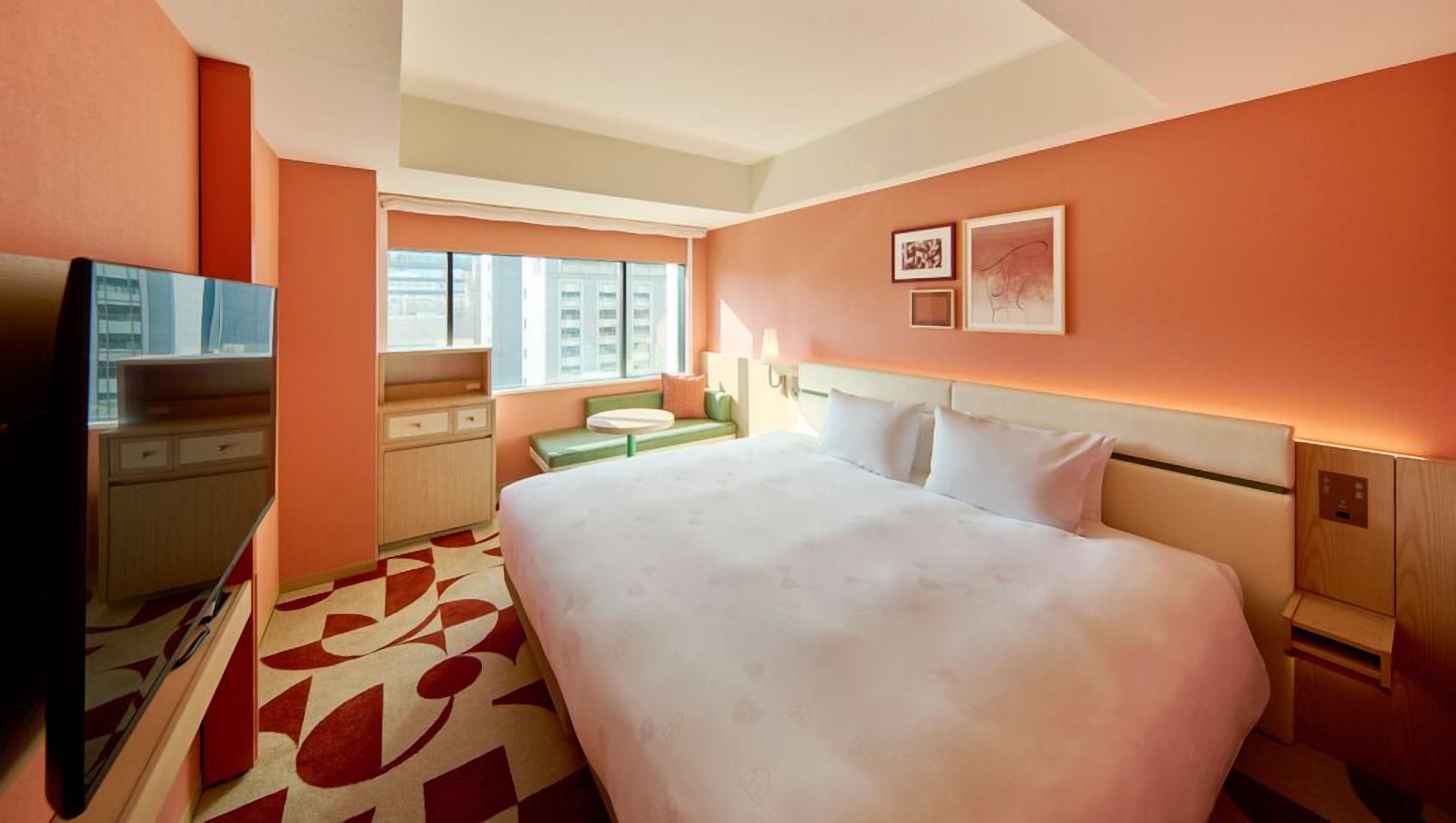 A hotel room with a bed, a desk, a television, a window, and artwork on the wall.