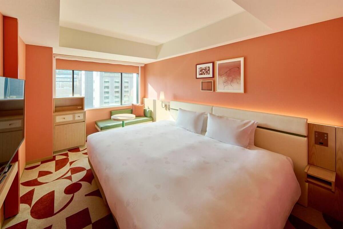 A hotel room with a bed, a desk, a television, a window, and artwork on the wall.