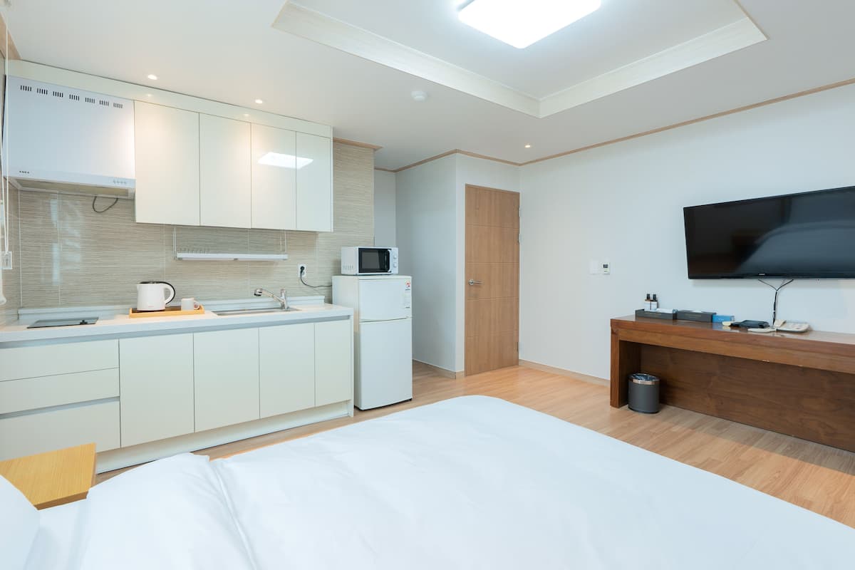 Moderni hotellihuone, jossa on pieni keittiö, sänky, televisio ja puinen työpöytä.