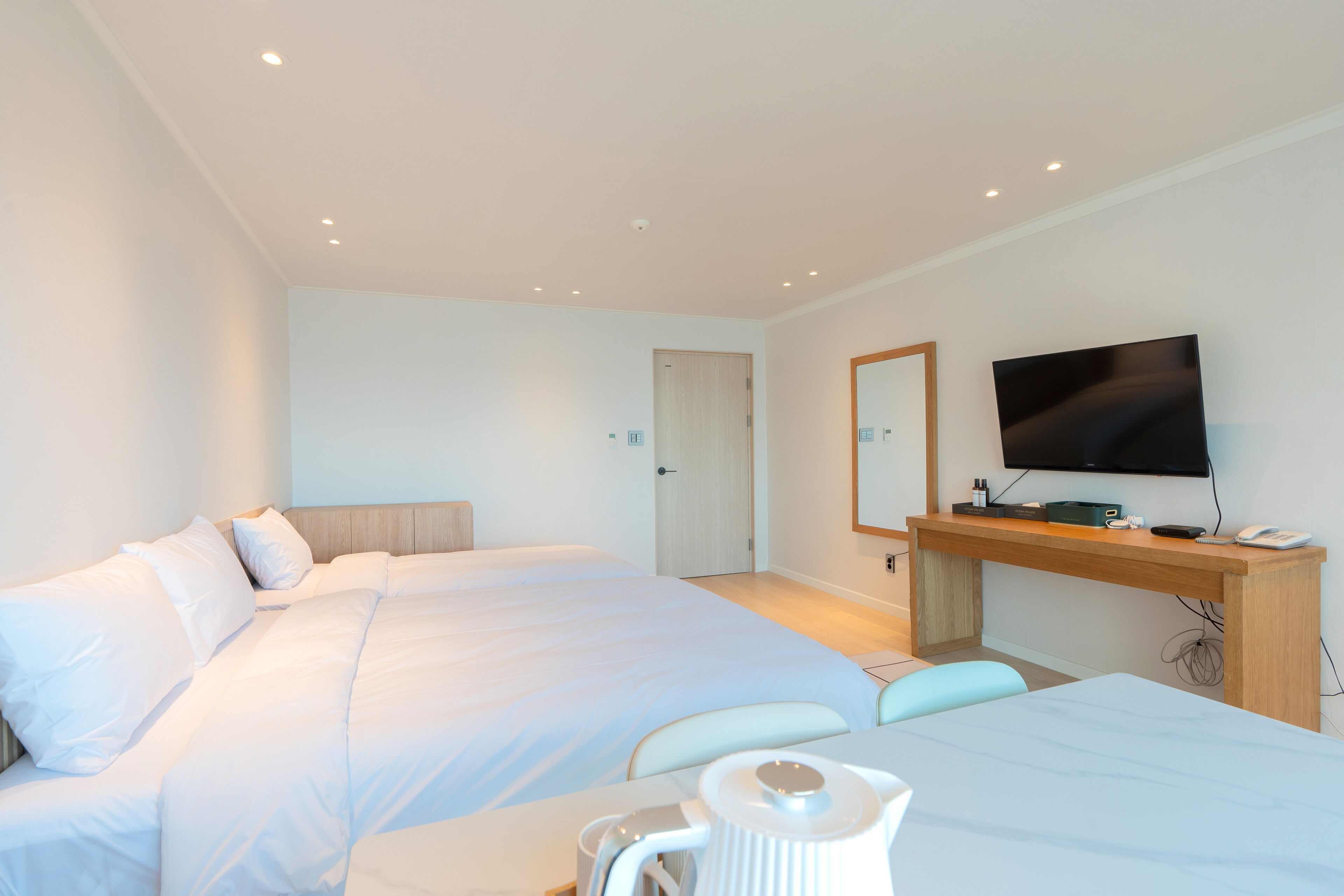 A modern hotel room with a large bed, a desk with a flat-screen TV, and a bathroom door.