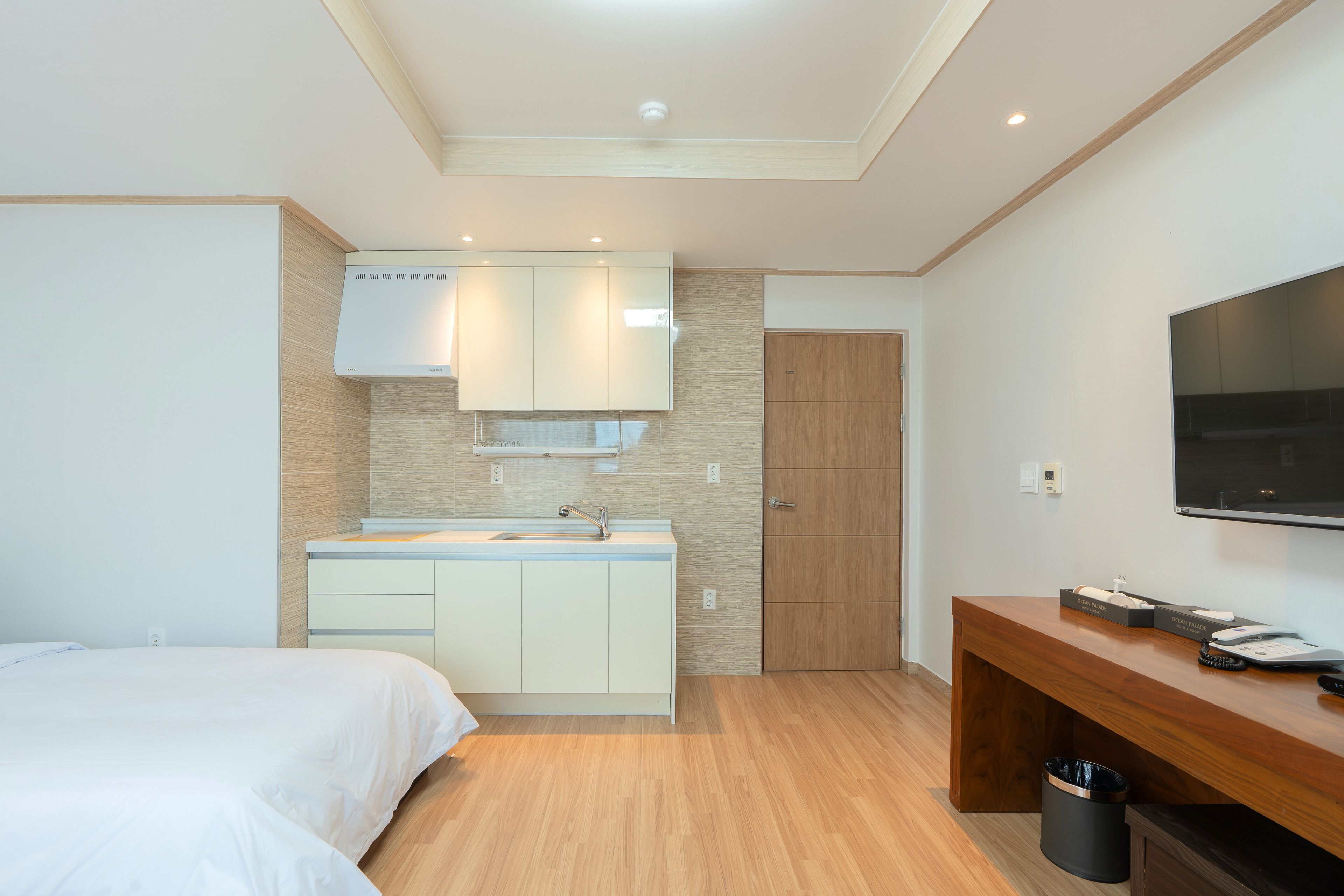 Una habitación de hotel moderna con cama, kitchenette, piso de madera, televisor y escritorio.
