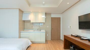 Una habitación de hotel moderna con cama, kitchenette, piso de madera, televisor y escritorio.