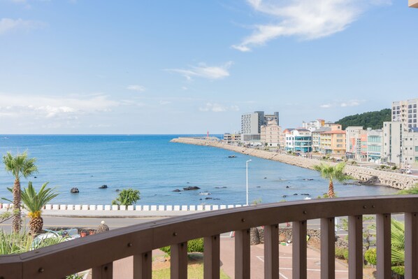 A coastal cityscape with buildings along the waterfront, a clear sky, and a view from a balcony with a railing. - Oceanpalade Hotel and Resort (Jeju City)