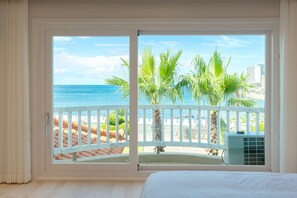 A room with a large window overlooking a beach, a balcony with a white railing, and an air conditioning unit. - Oceanpalade Hotel and Resort (Jeju City)
