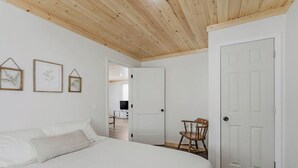 A bedroom with a bed, a wooden chair, and a door leading to another room.