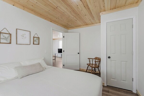 A bedroom with a bed, a wooden chair, and a door leading to another room.