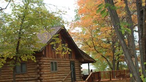 A log cabin with a porch and steps leading up to the entrance, surrounded by trees with autumn leaves. - LABOR DAY SALE-Private Trillium Lake Log Cabin-Sauna & Nature Escape (Hackensack)