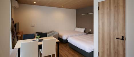 A modern room with a wooden ceiling, a desk with a chair, two beds, and a wardrobe.
