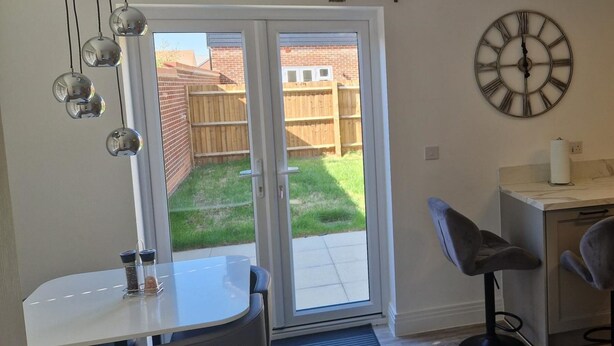A room with a sliding glass door leading to a backyard, a round wall clock, and a small table with a chair. - Peterborough - House - Sleeps 8 - Parking - Garden (Peterborough)