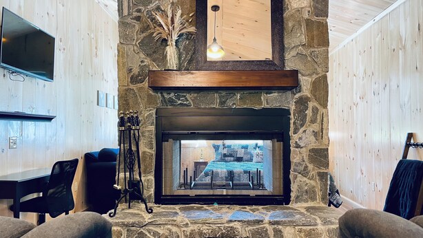 Una chimenea de piedra con un televisor montado encima, un repisa de madera y un colgante de luz.