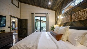 Une chambre avec un grand lit, des murs en bois, une télévision et une vue sur l’extérieur.