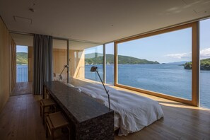 A modern bedroom with a large window overlooking a body of water and hills.