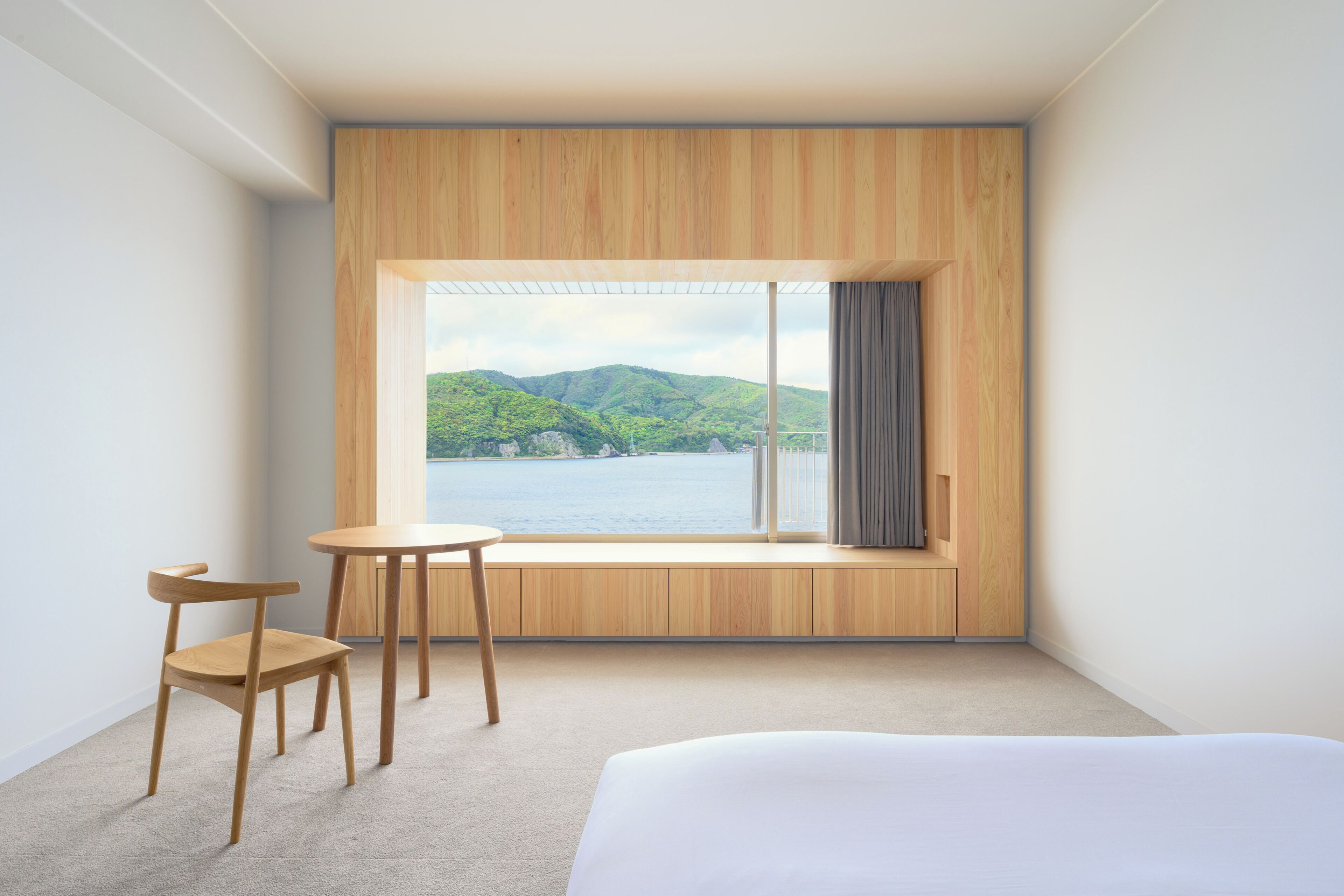 Una habitación de hotel con un ventanal grande, una cama, una mesita y una silla.