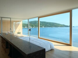 Una habitación moderna con una cama grande, una mesa larga y vistas al mar y las colinas.