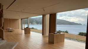 Una camera spaziosa con parquet, ampie finestre con vista su un lago e montagne, un divano e due tavolini in legno.