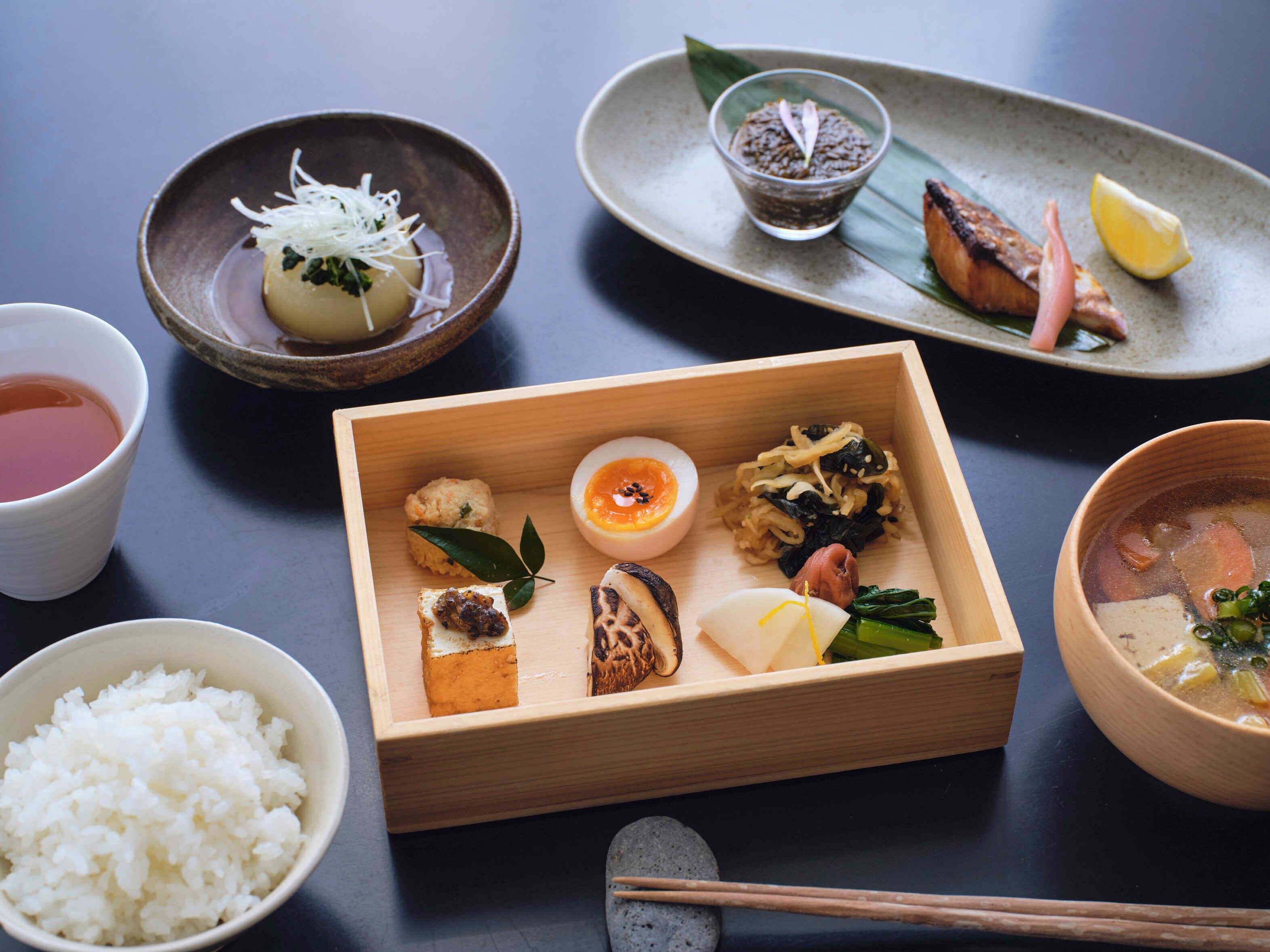 Eine Holzkiste mit verschiedenen japanischen Gerichten, Reis in einer Schüssel und einer Tasse Tee.