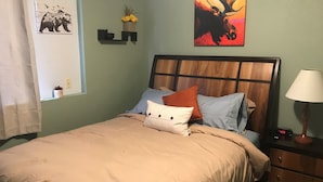 A neatly made bed with a beige comforter, a pillow, and a decorative pillow. A painting of a moose is on the wall above the bed. - Comfy 2 Bedroom 1 Bath Near Sand Lake and Airport (Anchorage)