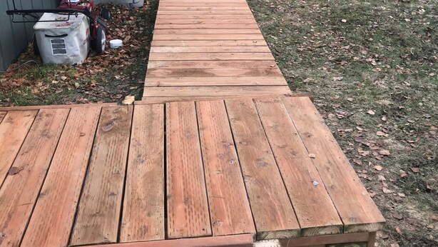 A wooden deck leading to a building with a metal fence and trees in the background. - Comfy 2 Bedroom 1 Bath Near Sand Lake and Airport (Anchorage)