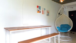 A room with a wooden bench, a hanging chair with blue cushions, and three abstract wall art pieces.