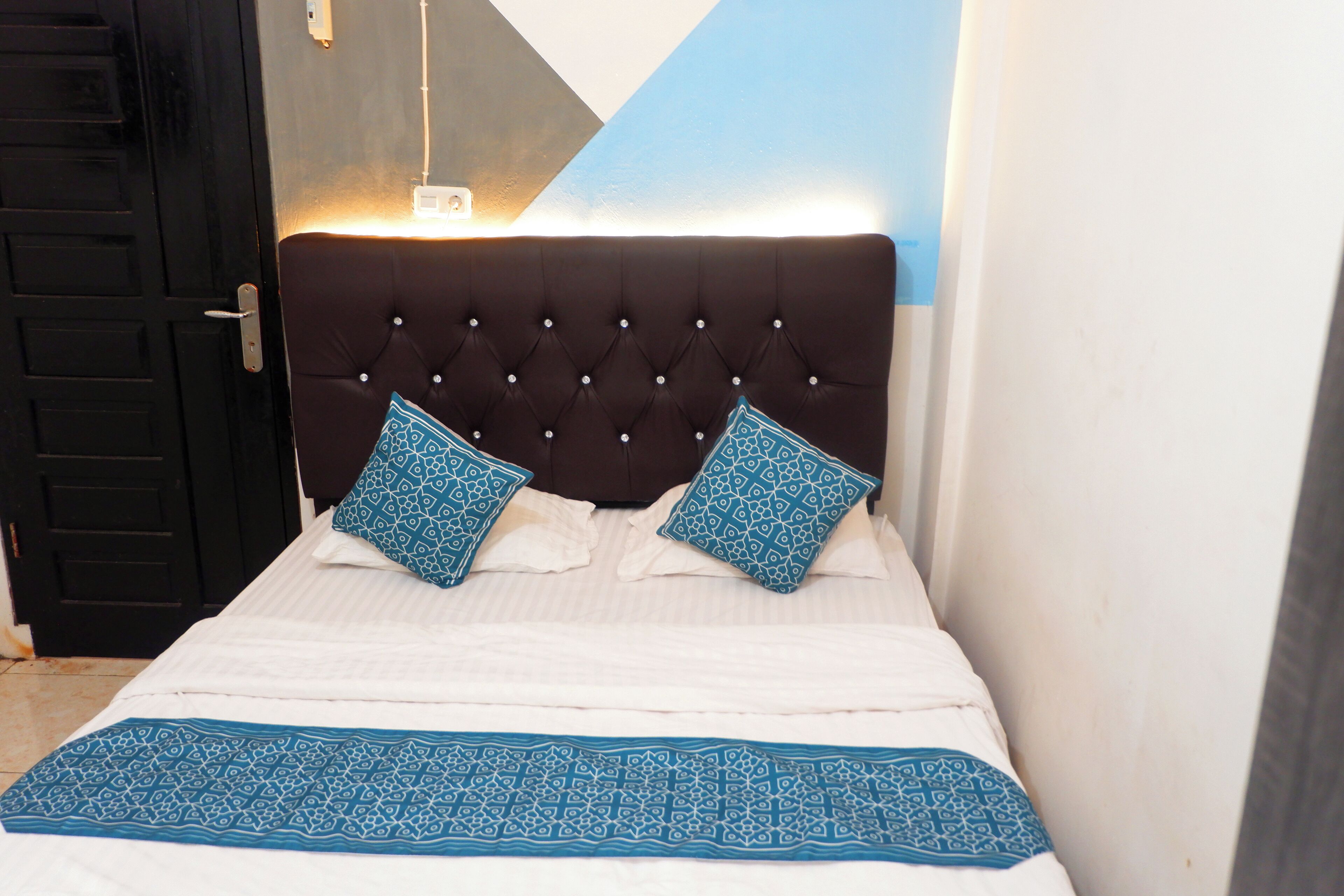 A bed with a tufted headboard, two patterned pillows, and a blue patterned bedspread.