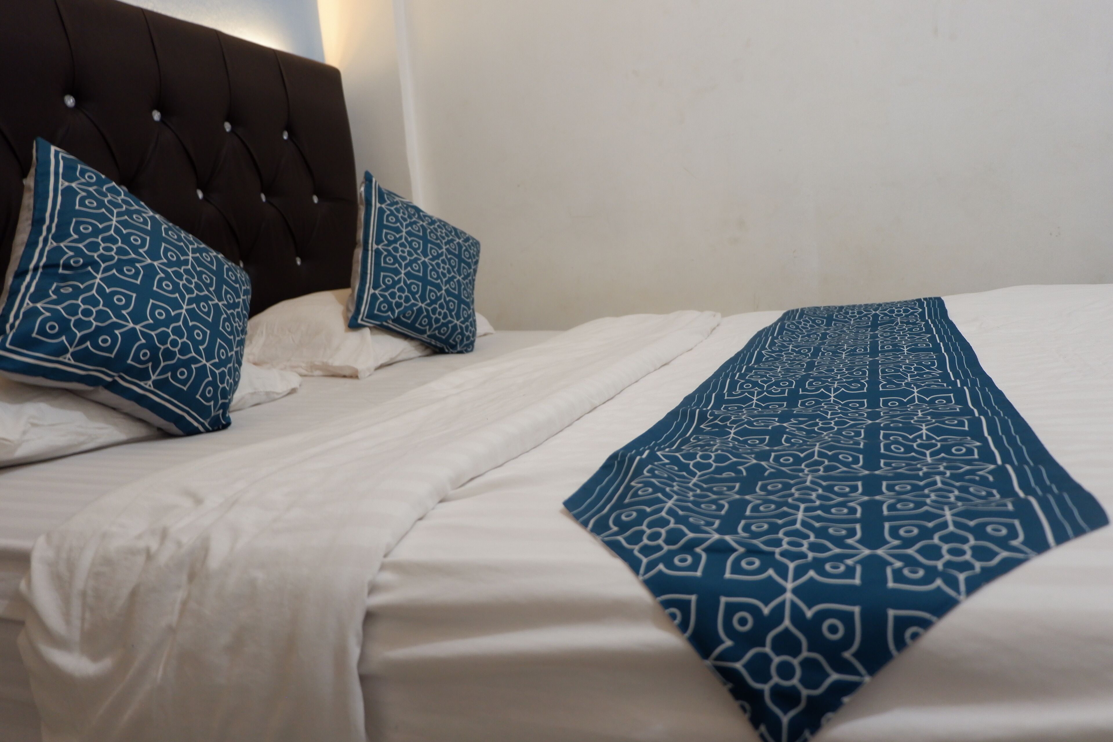 Un lit bien fait, avec du linge de lit blanc et des coussins et un couvre-lit à motifs bleus.
