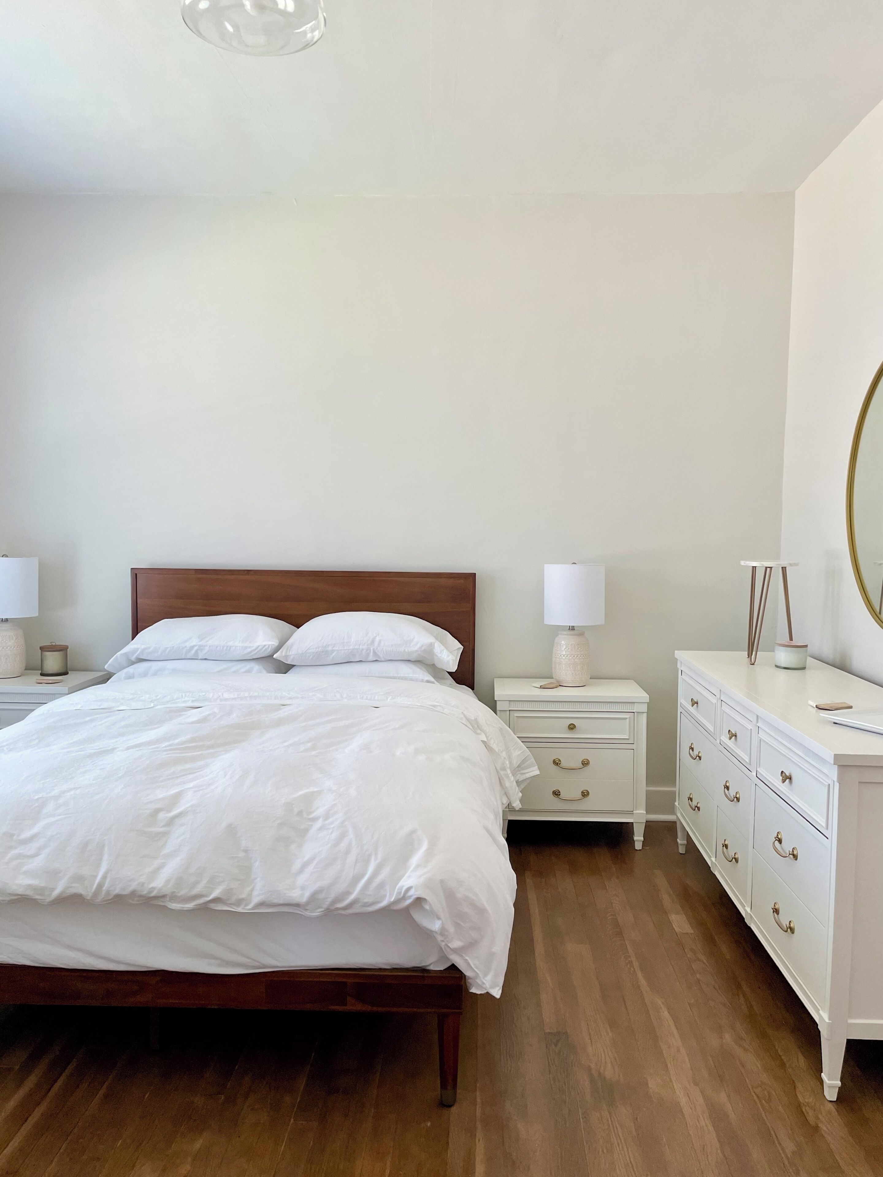Une chambre à coucher avec un lit en bois, des tables de chevet blanches, une commode et un miroir.