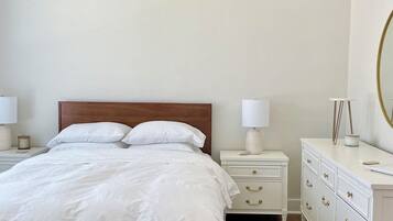 Une chambre à coucher avec un lit en bois, des tables de chevet blanches, une commode et un miroir.