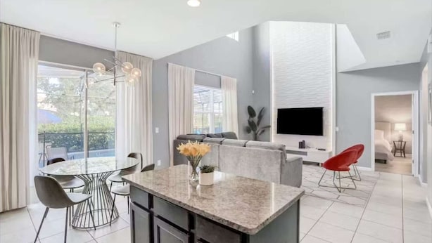 A modern living room with a TV, a dining area with a round table and chairs, and a kitchen area with a marble countertop. - Solterra Resort 6 bed home, 20 mins to Disney, 5 mins to Championsgate! (Davenport)