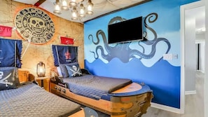 Una habitación con temática náutica, que incluye una cama con cabecera de timón de barco, un mural de pulpo en la pared y una bandera con calavera y huesos cruzados.