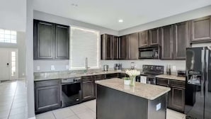A modern kitchen with dark wood cabinets, a granite countertop, stainless steel appliances, and a large window providing natural light. - Solterra Resort 6 bed home, 20 mins to Disney, 5 mins to Championsgate! (Davenport)