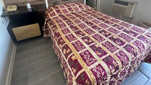 A bedroom with a wooden headboard, a bed with a patterned bedspread, a bedside table with a telephone, and a radiator. - Travel Inn (Montgomery)