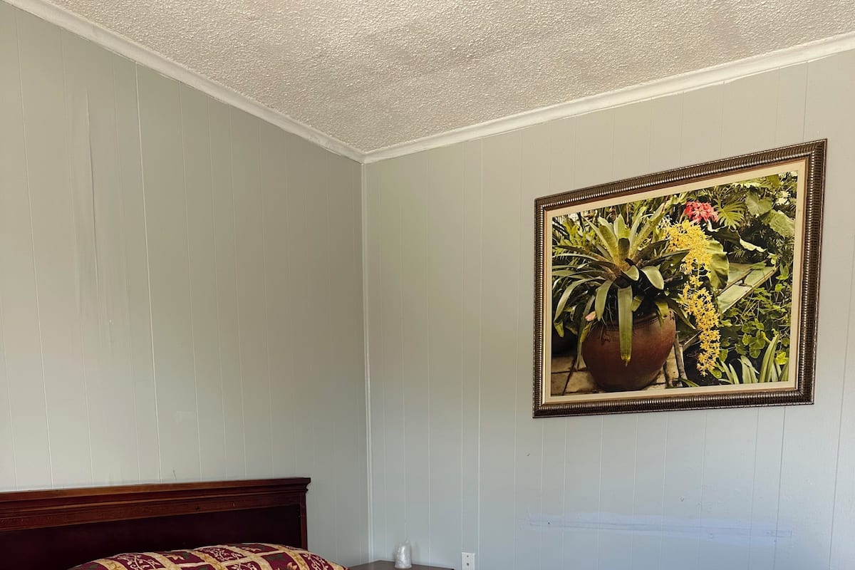 Una cama bien hecha con una colcha estampada, un cabecero de madera y un cuadro de una planta colgado en la pared.