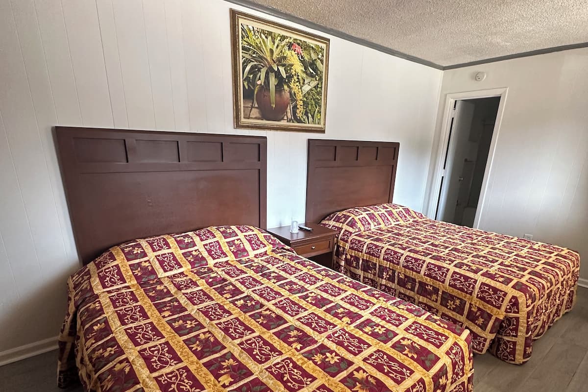 Habitación de hotel con dos camas, cada una con una colcha estampada, una mesita de noche, un cuadro enmarcado en la pared y una puerta que da a otra habitación.