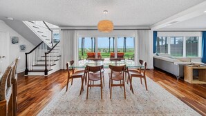 A spacious living room with a glass dining table, wooden chairs, a staircase, and a view of the outdoors. - Dream Beach Home Vacation - Direct Beach Access & Exquisite Waterfront Views (Cocoa Beach)