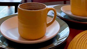 Una taza amarilla sobre un plato, otra taza sobre un plato, una mesa, una silla y un sofá con cojines.