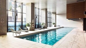 Una piscina interior con paredes de vidrio transparente, sillones de descanso y plantas en macetas.