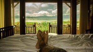 A bed with a view of a beach and mountains through open windows. - Villa Kedisan Lake View Kintamani (Kintamani)