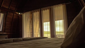 A room with a bed, a wooden headboard, and a window with sheer curtains. - Villa Kedisan Lake View Kintamani (Kintamani)