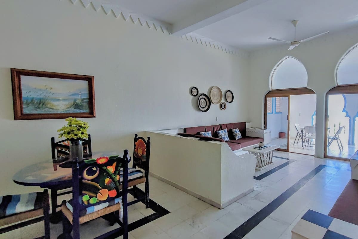 A spacious living area with a sofa, a dining table with chairs, and a ceiling fan.