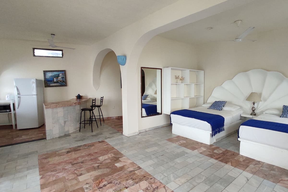 A hotel room with two beds, a small kitchenette, a dining area, and a bathroom.