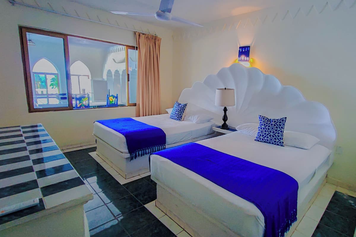 A hotel room with two beds, a checkered table, and a view of a building through a window.