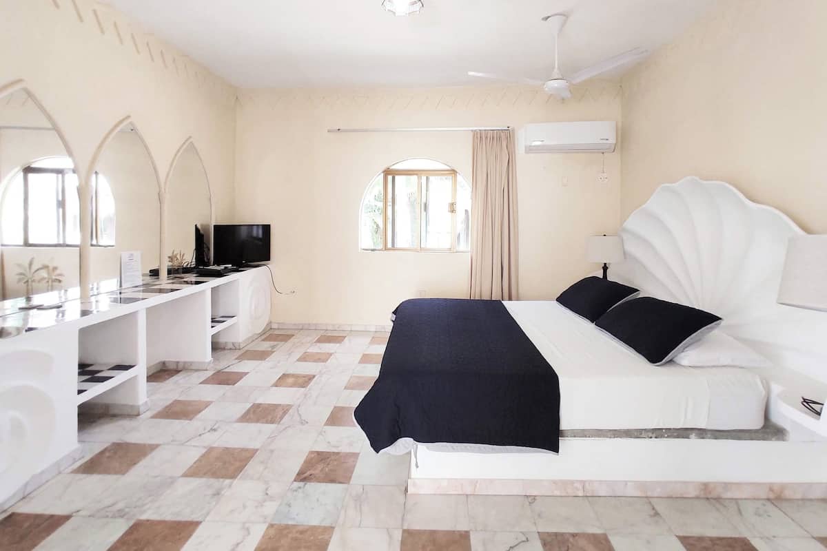 A hotel room with a bed, a TV, a desk, and a window.