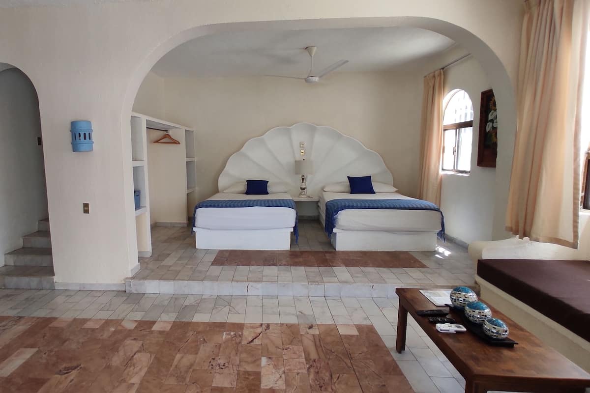 A hotel room with two beds, a wooden table, and a ceiling fan.