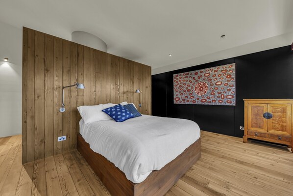 A modern bedroom with a wooden bed, a nightstand, a wall-mounted lamp, and a decorative wall piece. - 24 Hill Street - Pet friendly (Merimbula)