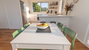 A modern kitchen with a white table, green chairs, and a bowl of fruit. - Lochview - Pet Friendly Merimbula (Merimbula)