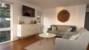 A modern living room with a grey sofa, a white sideboard, a round coffee table, and a large TV mounted on the wall. - Lochview - Pet Friendly Merimbula (Merimbula)
