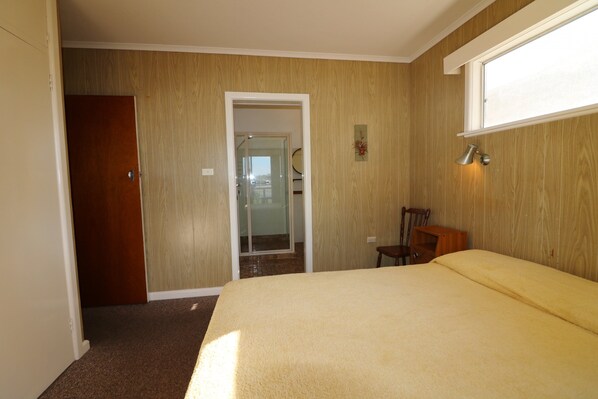 A bedroom with a bed, a wooden door, a chair, and a window. - Osborne House (Merimbula)