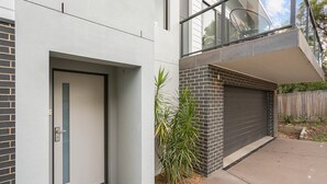 Une maison moderne à deux étages, dotée d’un portail de garage, d’une porte avec une poignée et d’un petit jardin agrémenté de plantes.