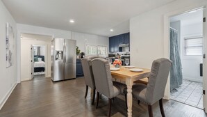 A modern kitchen with stainless steel appliances, a dining area with a wooden table and gray upholstered chairs, and a hallway leading to a bedroom. - Walk to Downtown~3 King Beds~Private Office (Raleigh)